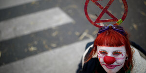 Eine junge Frau mit aufgemaltem Clownsgesicht und einer Pappsanduhr auf dem Kopf