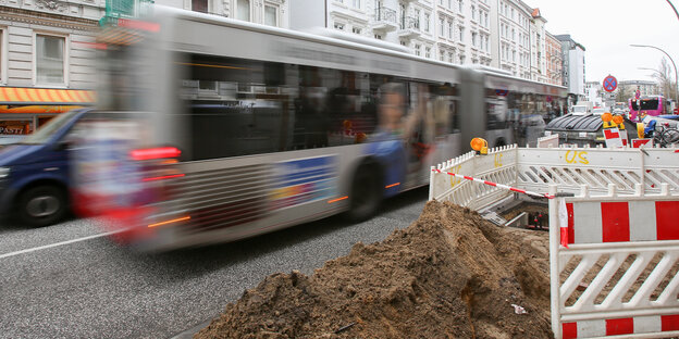 Ein verwischter Bus fährt an einem Sandhaufen mit Baustellenabsperrung vorbei.