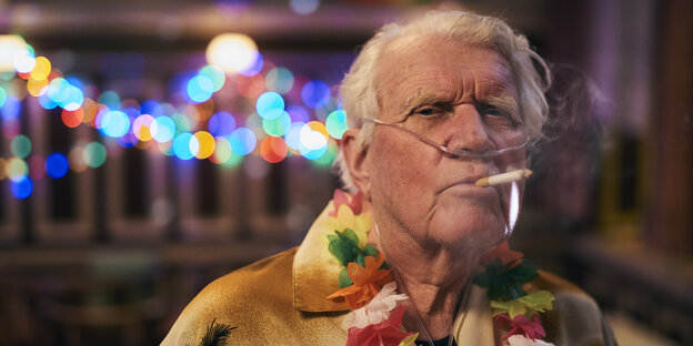 Ein alter Mann beim Rauchen, im Hintergrund Partybeleuchtung