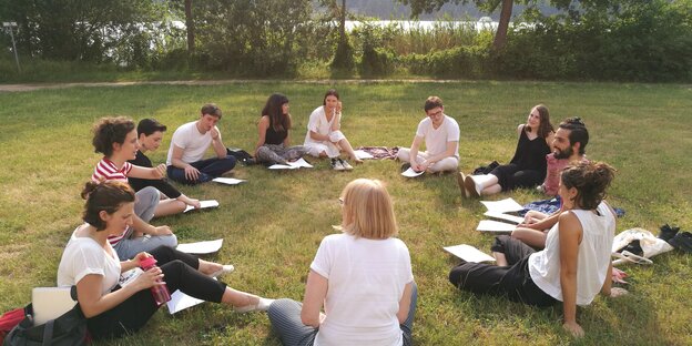 Mehrere Stipendiat*innen sitzen auf einer Wiese vor einem Teich im Kreis