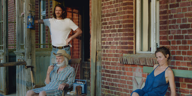 Ein alter und ein junger Mann und eine junge Frau sitzen auf der Veranda vor dem Haus
