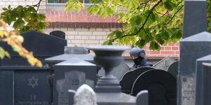 Polizist mit Helm steht zwischen Grabsteinen auf dem jüdischen Friedhof in Halle