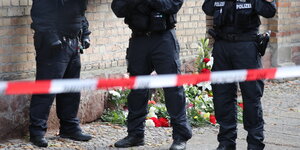 Polizisten hinter einem Absperrband vor der Synagoge in HAlle, dahinter Blumen an der Gebäudemauer