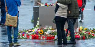 Passanten stehen am Marktplatz an niedergelegten Blumen