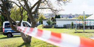 Ein Polizeiauto steht hinter eibnem Baum, davor Absperrband und Wiese