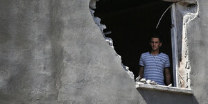 Ein Mann blickt durch ein Loch aus einem Haus heraus, das bombardiert wurde.