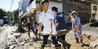 Menschen reinigen eine Straße, nachdem ihre Stadt aufgrund des Taifuns überschwemmt wurde. Im Vordergrund schaufelt ein Junge.