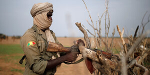 Ein Soldat der malischen Streitkräfte hält ein Gewehr in der Hand, das halb von Sträuchern verdeckt wird