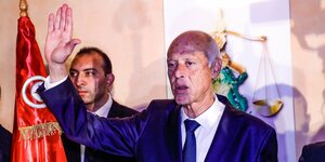 Kais Saled, Wahlsieger von Tunesien hebt die Hand vor der Landesflagge