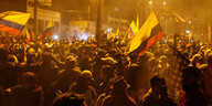 Viele Menschen mit gelb-blau-roten Ecuador-Fahnen stehen in der Nacht auf einem Platz.