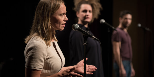 Zwei Frauen und ein Mann stehen vor Mikrofonen auf der Bühne