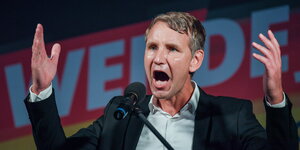 ein Mann steht mit aufgerissenem Mund und erhobenen Händen vor einem Mikrofon