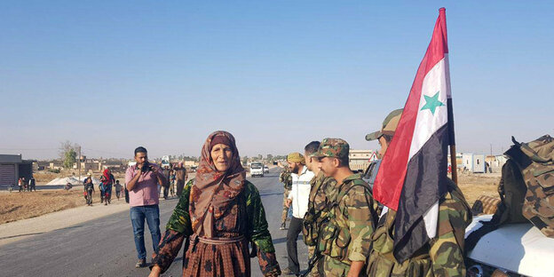 Zu sehen ist eine Frau neben syrischen Soldaten, die nun in die nördliche Stadt Tal Tamr eingezogen sind