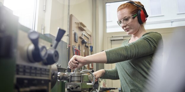 Frau mit Ohrenschützern an einer Werkbank