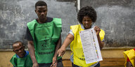 Eine Frau und zwei Männer gestikulieren mit Wahlzetteln in der Hand.
