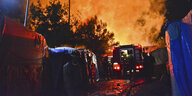 Ein Feuerwehrauto steht Nachts zwischen Zelten und vor einem von Flammen erleuchteten Himmel