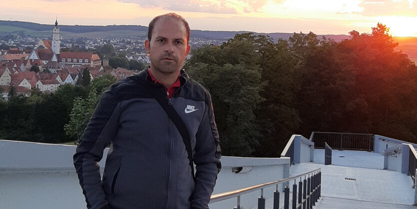 Murat Akgül steht mit den Händen in den Hosentaschen vor einer Landschaft mit untergehender Sonne