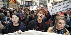 Drei Jugendliche auf einer Demo von Fridays for Future halten ein Transparent und rufen etwas