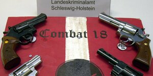 Vier Waffen liegen vier Waffen, der Schriftzug vom "Combat 18" ist zu sehen. Im Hintergrund steht ein Schild mit "Landeskriminalamt Schleswig-Holstein"