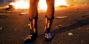 Stiefel in den Farben der katalanischen Flagge dekoriert und nackte Beine vor Flammen