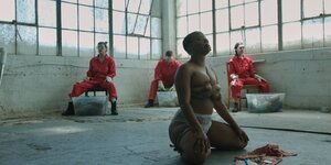 Eine Frau sitzt fast nackt mit Seilen verpackt in einer Industriehalle - eine Szene aus dem Porno "W/HOLE"