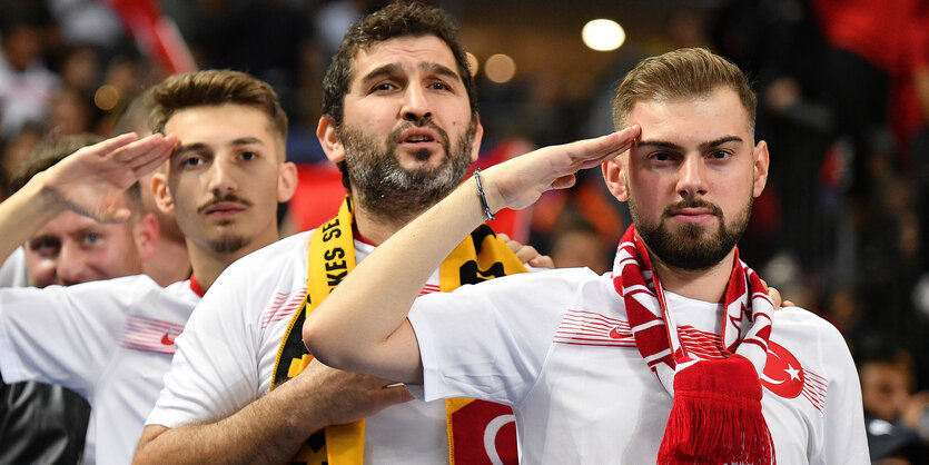 Drei Fans salutieren auf der Tribüne