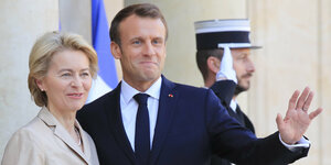 Ursula von der Leyen und Emmanuel Macron stehen vor dem Elysée-Palast, Macron winkt.