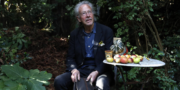 Mann sitzt in einem Garten, hält einen Hut in der Hand , auf einem Tisch liegen Äpfel
