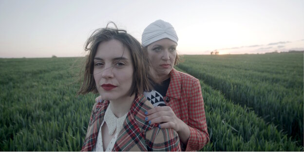 Zwei Frauen stehen, die eine hinter der anderen, inmitten eines grünen Feldes.