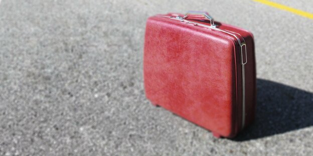Eine roter Koffer steht auf einer Straße