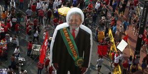 Über einer Menschenmenge mit Protestplakaten steht die Gummifigur des Ex-Präsidenten Lula da Silva
