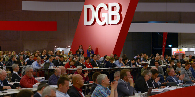 Ein Saal voller Menschen an Tischen, im Hintergrund das DGB-Logo