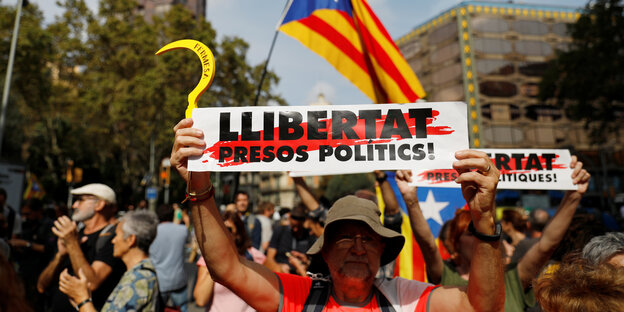 Eine ältere Frau hält ein Schild in die Höhe. Im Hintergrund katalanische Fahnen.