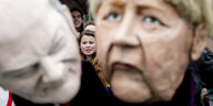 Menschen protestieren mit Masken von Merkel und Scholz
