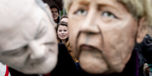 Menschen protestieren mit Masken von Merkel und Scholz