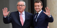 Emmanuel Macron und Jean-Claude Juncker winken Arm in Arm in die Kamera.