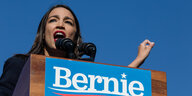 Eine Frau reckt kämpferisch die Faust, sie steht hinter einem Rednerpult mit dem Banner Bernie Sanders