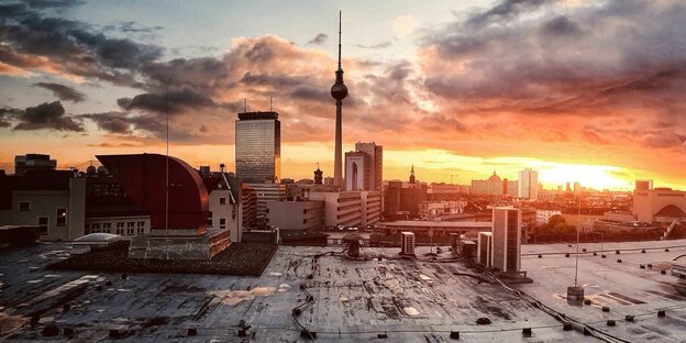Der Berliner Fernsehturms vor einem gold glühenden Abendhimmel, im Vordergrund eine Bracheund umliegender Häuser