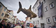Demonstranten halten einen Plüschhai an einem Stock in die Luft.