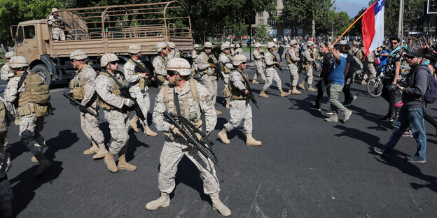Chilenische Soldaten stehen Wache während Demonstranten mit Fahnen protestieren