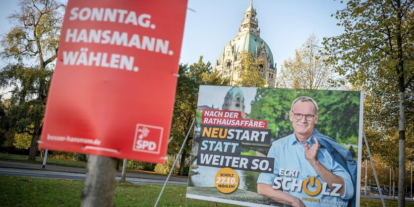 Im Vordergrund Wahlplakate, im Hintergrund Bäume und ein Gebäude.