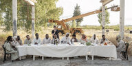 Viele schwarze Menschen sitzen um einen Tisch, es sieht aus wie die Darstellung des Abendmahl von Jesus mit den zwölf Aposteln, in der Mitte steht der Schweizer Regisseur Milo Rau.