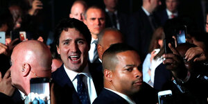 Justin Trudeau steht in einer Menschenmeng, lacht, neben ihm zwei Bodyguards