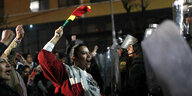 Eine Frau mit einer bunten Fahne steht vor Polizisten