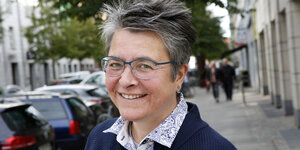 Portraitbild von Monika Herrmann, Kreuzberger Bürgermeisterin. Sie steht auf einer Straße und lachtlacht in die Kamera