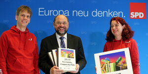 Martin Schulz im Anzug präsentiert die Bücher mit den Unterschriften, links von ihm in Rot Felix Kolb