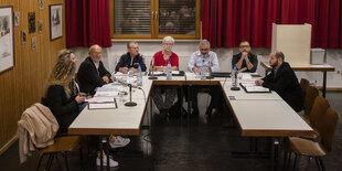 Jüngere und ältere Menschen sitzen an einem langen u-förmigen Tisch