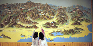 Zwei Menschen zeigen auf eine an der Wand hängende Karte von einem Gebirge.