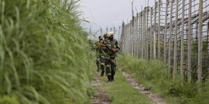 Bewaffnete Soldaten laufen an einem Zaun entlang