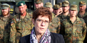 Annegret Kramp-Karrenbauer trägt einen violetten Schal und steht vor einer Truppe Bundeswehrsoldaten